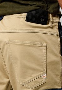 Shorts beige avec une poche arrière, une taille texturée noire et des accents en denim contrastés. Comprend une petite étiquette logo sur la taille.