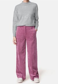 Grå stickad tröja med paljettrand, i kombination med vida, ljusrosa kordbyxor. Vita sneakers fulländar outfiten.