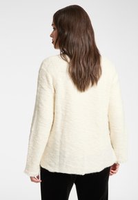 Witte gestructureerde jas met een losse pasvorm, voorzien van een ronde halslijn en rafelige mouwzomen, gezien van achteren.