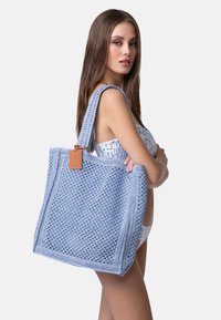 Borsa tote intrecciata di colore azzurro chiaro con design testurizzato e spallacci robusti. Presenta un'etichetta in pelle attaccata con un cordino.