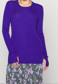 Ribbad, långärmad tröja i stark lila, med rundad hals och tumhål, i kombination med en blommönstrad kjol.