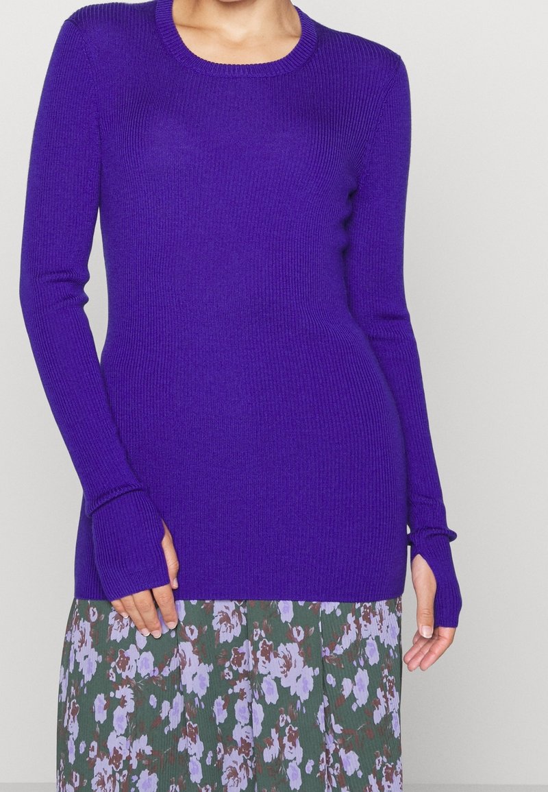 Ribbad, långärmad tröja i stark lila, med rundad hals och tumhål, i kombination med en blommönstrad kjol.