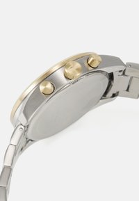 Montre en métal dotée d'un bracelet en acier inoxydable argenté, d'accents dorés sur la lunette et les boutons-poussoirs, et d'un design de boîtier rond élégant.