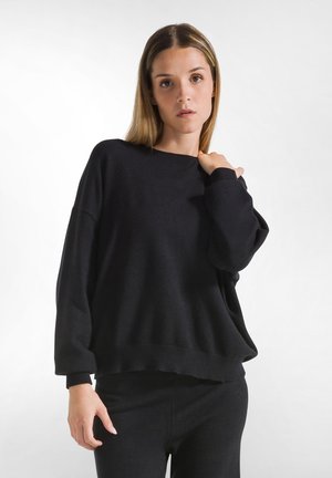 Zwarte oversized trui met lange mouwen, geribbelde manchetten en zoom. Zachte textuur, ronde halslijn, gedragen met bijpassende zwarte onderkleding.