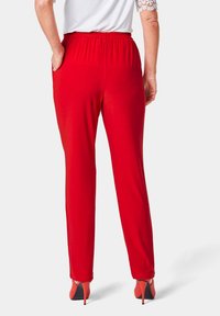 Pantalon rouge à taille élastique avec une texture lisse, design à jambe droite et poches latérales. Porté avec des chaussures à talons, vu de derrière.