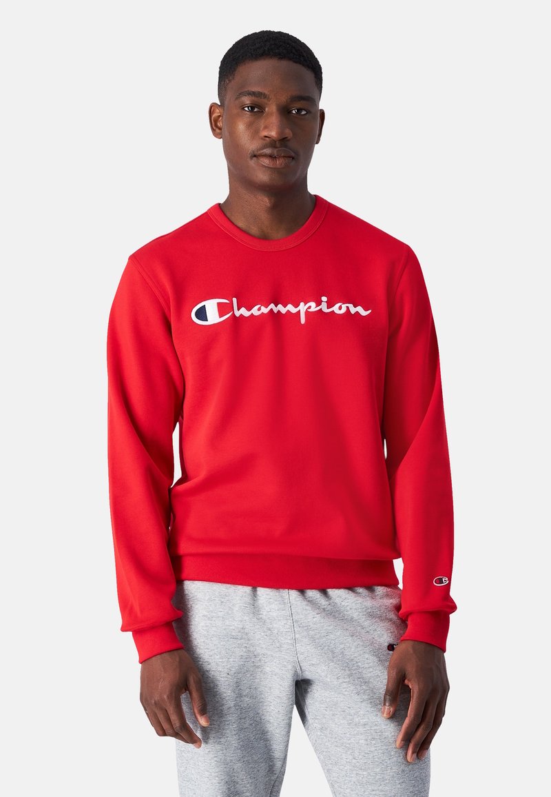 Sudadera roja hecha de una mezcla de algodón, con un cuello redondo y puños acanalados, con un logo blanco de "Champion" en el frente.