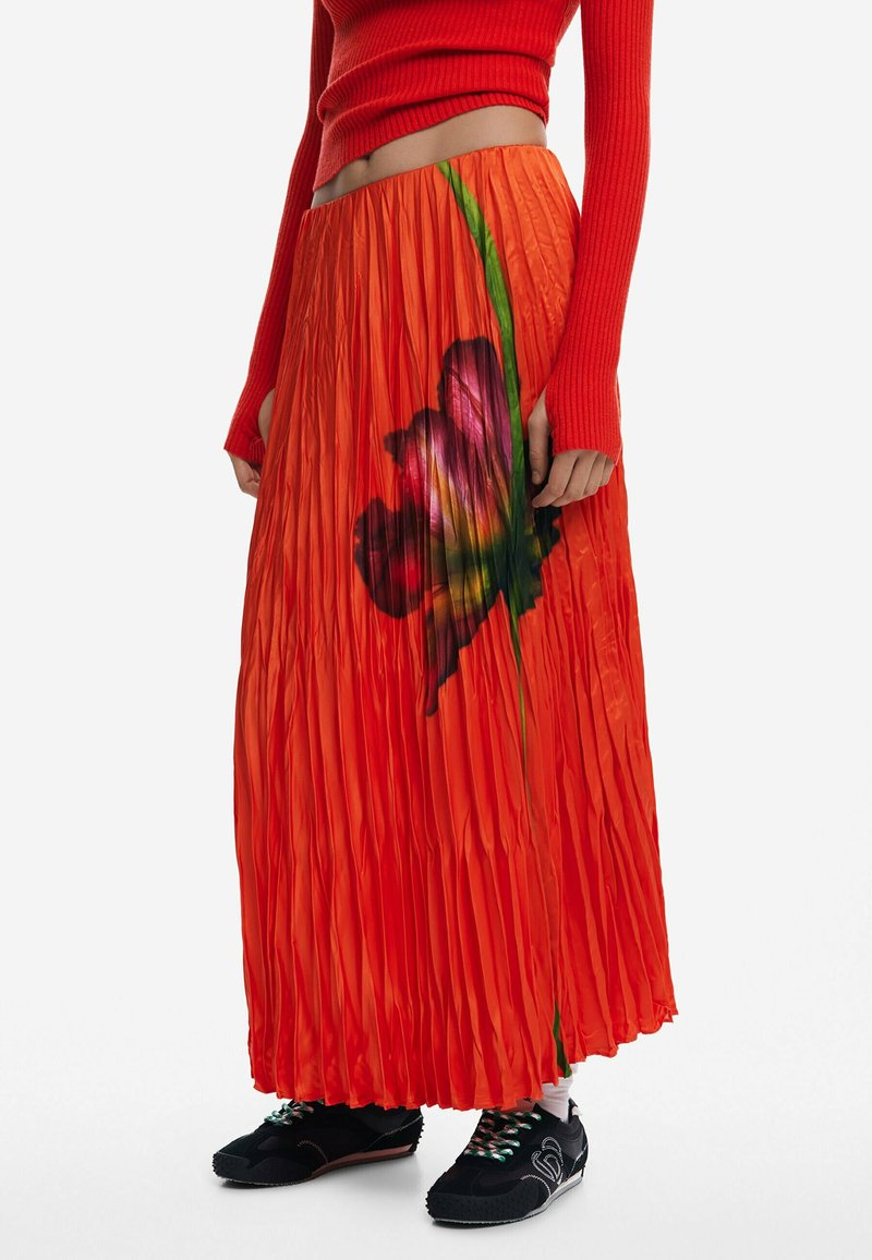 Jupe plissée rouge ornée d'un grand motif floral coloré. Fabriquée dans un matériau brillant, elle possède une silhouette fluide et une taille élastique.