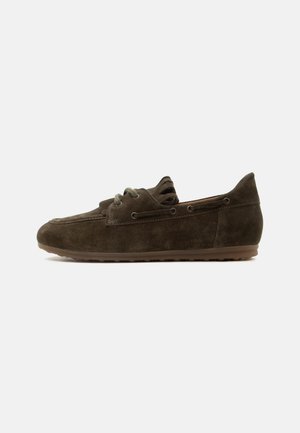 Mocassin en daim brun foncé avec détail en lacet et semelle en caoutchouc, présenté de côté sur un fond clair uni.