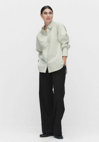 Striped button-up shirt in light green and white, featuring long sleeves, relaxed fit, paired with black wide-leg trousers and black shoes.