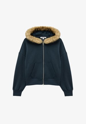 Marineblå hættetrøje med lynlås, forlommer og beige imiteret pelskant rundt om hætten, vist på hvid baggrund.