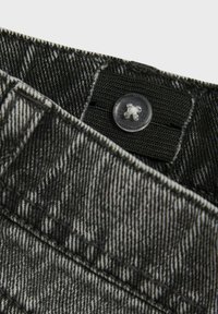 Denim tkanina s crno-bijelim prugama, s vidljivim kopčanjem na dugme i šivenim detaljima na pojasu. Prikaz iz blizine ističe teksturu.