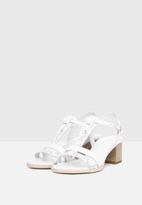 Sandali con tacco bianco, caratterizzati da design con ritagli, cinturini texturizzati, fibbie regolabili e un tacco in legno. Sole liscia e di colore chiaro.
