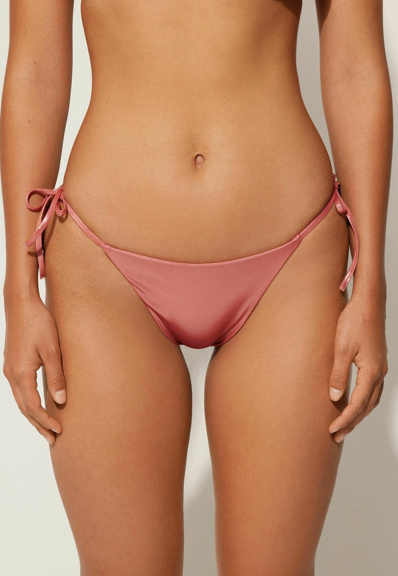 Růžové bikiny s nastavovacími šňůrkami na každé straně, vyrobené z hladkého, pružného materiálu, s minimalistickým designem a nízkým pasem.