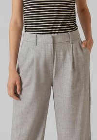 Pantalons plissés gris clair en tissu texturé, dotés de poches latérales et d'une ceinture, associés à un top à rayures noir et blanc.
