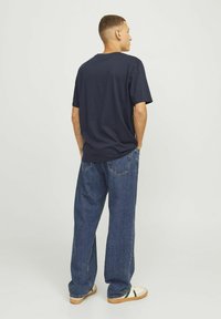 Marineblå t-shirt med rund halslinning, parret med løstsiddende blå jeans, der viser en glat tekstur og afslappet design.