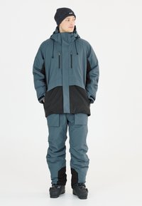 Wasserdichte Outdoor-Jacke und Hose im Dunkelblau mit schwarzen Akzenten. Merkmale sind eine verstellbare Kapuze, Reißverschlusstaschen und eine lockere Passform für Beweglichkeit.