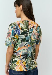 Blouse à manches courtes avec un imprimé tropical multicolore, dotée d'un col rond, d'un tissu texturé et d'une fente au dos avec un détail de bouton.