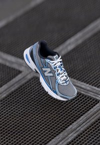 Chaussure de sport pour hommes en maille grise avec des touches bleues et blanches, dotée d'un col rembourré, de lacets blancs et d'une semelle amortie.