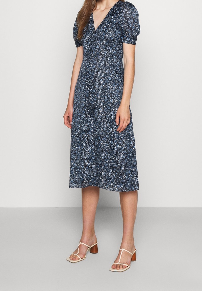 Vestido midi de estampado floral en azul marino con mangas abullonadas, escote en V y falda fluida. Combinado con sandalias de tacón beige.