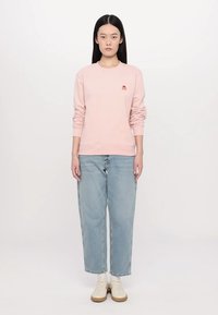 Lyserød sweatshirt med ribbede manchetter og kant, prydet med et lille rødt logo. Sammen med løse lyseblå denimjeans og hvide sneakers.