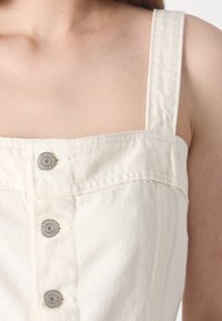 Vit denimtop med fyrkantig halsringning, smala axelremmar och silverfärgade tryckknappar framtill. Mjuk textur och figursydd design.