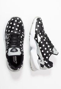 Svarta sneakers med stora vita prickar, med grå detaljer, en vadderad tunga och svarta snören. Tjock gummisula för stöd.