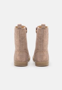 Botines de ante rosa con un acabado texturizado, que presentan tachuelas decorativas a lo largo de la parte inferior y pequeñas hebillas decorativas en los lados.
