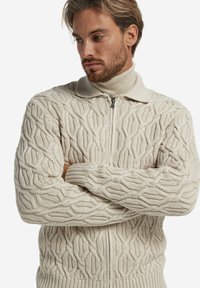Beige gestrickter Reißverschluss-Pullover mit strukturiertem Blattmuster, Rippbündchen und einem hohen Kragen für zusätzlichen Wärme- und Stil.