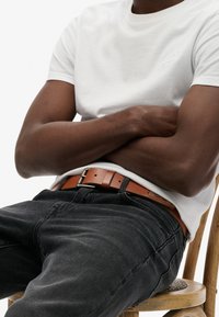 Biała bawełniana koszulka z okrągłym dekoltem, zestawiona z ciemnoszarymi dżinsami i brązowym skórzanym paskiem z srebrną klamrą.