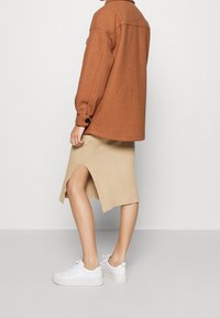 Brun fleecejakke, ribbet beige strikket nederdel med sideslids og hvide sneakers. Bløde teksturer, afslappet pasform og casual design.