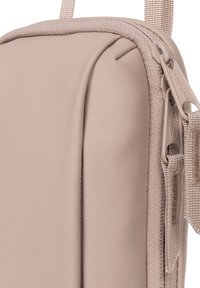 Sac en softshell beige, avec une texture lisse, de forme rectangulaire plate et une fermeture éclair. Il comprend une bandoulière en tissu durable et des accents matériels minimalistes.