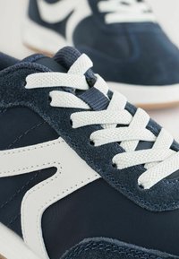 Marine sneakers met witte accenten, gemaakt van suede en ademend mesh, met platte witte veters en een textuur rubberen zool.