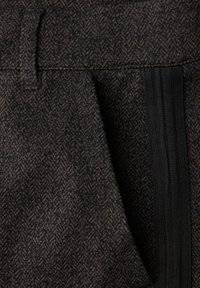 Brązowa tkanina w jodełkę o fakturowanym wyglądzie. Zawiera czarny elastyczny pasek i pętlę na pasie dla bezpiecznego zapięcia.