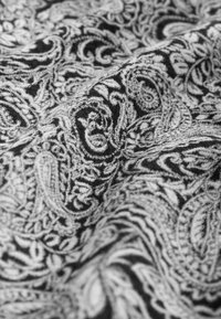 Tessuto nero con intricati motivi paisley bianchi, caratterizzati da varie forme a spirale e texture dettagliate, che creano un ricco contrasto visivo.