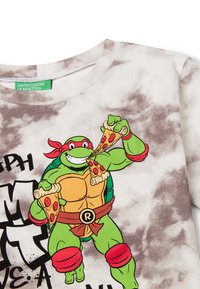 Bílo-šedé tričko s tie-dye vzorem, na kterém je grafika zelené kreslené želvy s červenými detaily, která drží dva plátky pizzy, a černý text.