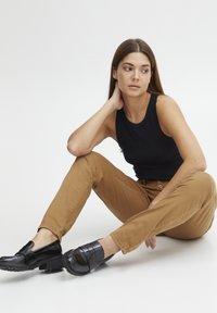 Haut sans manches noir, pantalon marron ajusté et mocassins noirs brillants avec des accents texturés. Tissu lisse et coupe décontractée.