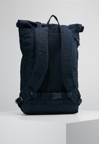 Námořnická modrá rolovací batoh, odolná tkanina, polstrované ramenní popruhy, boční zipová kapsa, nastavitelné spony, minimalistický design.