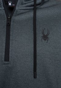 Felpa grigia scura con mezza zip, caratterizzata da un logo a ragno nero sul petto e un tessuto testurizzato. Include cordini neri.