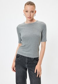 Grijze geribbelde top met korte mouwen, ronde halslijn, zachte textuur. Gecombineerd met hooggeplaatsen zwarte jeans met gebogen zakken en vervaagde details.