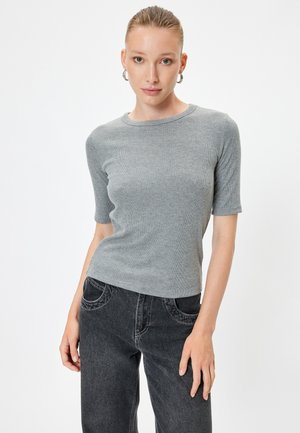 Grijze geribbelde top met korte mouwen, ronde halslijn, zachte textuur. Gecombineerd met hooggeplaatsen zwarte jeans met gebogen zakken en vervaagde details.