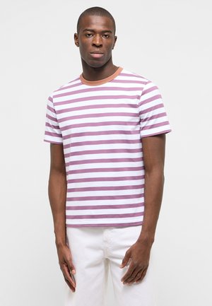 Mann trägt ein kurzärmeliges weiß-lavendelfarbenes T-Shirt mit horizontalen Streifen und weiße Hose, steht vor einfachem Hintergrund.