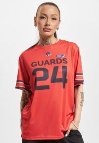 Rød kortermet trøye med "GUARDS 24" i marineblått, med hvite striper på ermene og et merke på øvre venstre side.