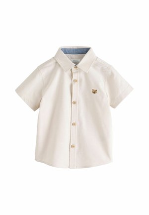 Chemise crème à manches courtes pour tout-petit, boutonnée, avec un petit visage d'ours brun brodé sur le côté gauche de la poitrine et une doublure de col intérieure bleue.