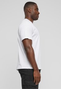 Hvid bomulds t-shirt med korte ærmer, rund halsudskæring og en almindelig pasform, båret med mørke cargo bukser. Enkel og ensartet design.