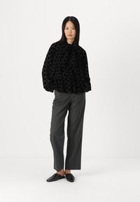 Black polka dot blouse with ruffled layers and a bow tie at the neck, paired with gray pinstripe trousers and black slip-on shoes.