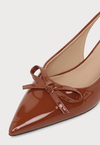 Λεπτό, καφέ γυαλιστερό παπούτσι slingback με διακοσμητικό φιόγκο στην κορυφή και μπεζ εσωτερική επένδυση.