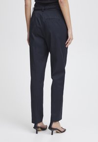 Pantaloni a sigaretta blu navy con una cintura intrecciata, dotati di tasca posteriore, texture liscia e orlo cropped sopra la caviglia.