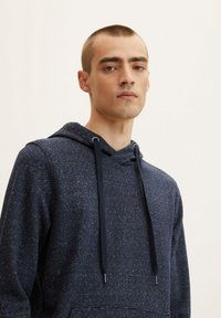 Sudadera azul marino con un patrón texturizado de finas rayas claras. Cuenta con una capucha con cordón y acentos metálicos en los extremos del cordón.