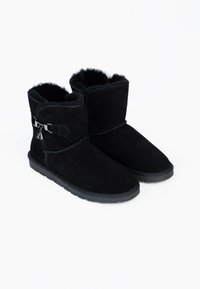 Botas de tobillo de ante negro con forro de piel sintética, que presentan una correa y un acento metálico. Las suelas son planas con un agarre texturizado.