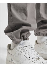 Pantalons à poignets élastiques gris associés à des baskets en cuir blanches avec des détails perforés, des lacets et une marque discrète sur la languette.